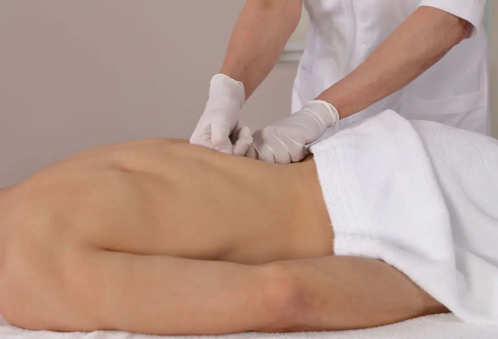 Muscular Man having Chiropractic Back Adjustment . Back pain relief, Injury Rehabilitation. Physiotherapy During the COVID-19 Pandemic, following Safety protocols Chiropractor in Clifton NJ providing spinal adjustment for pain relief in a modern clinic setting